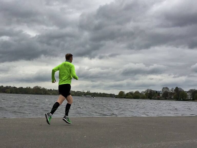 Ein Läufer in leuchtend grünem Shirt joggt am Wasser entlang, umgeben von einer lebhaften Landschaft. Marathon laufen macht glücklich!