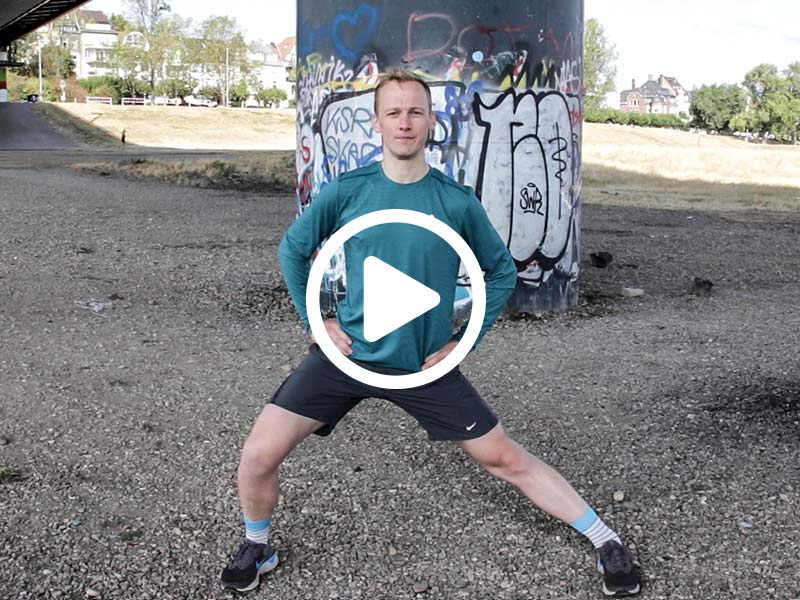 Lauftrainer Kevin zeigt eine Dehnübung für die Adduktoren