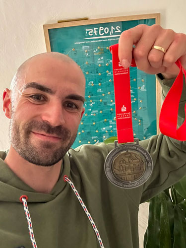 Ein glücklicher Läufer hält stolz seine Medaille nach einem erfolgreichen Rennen in einem hellen Raum.