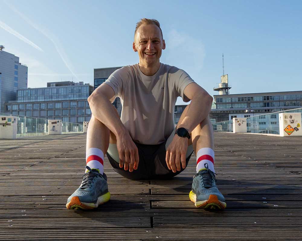 Ein fröhlicher Läufer sitzt auf einem Holzdeck, bereit für das nächste Abenteuer im Freien. Sportliche Kleidung und motivierte Ausstrahlung.