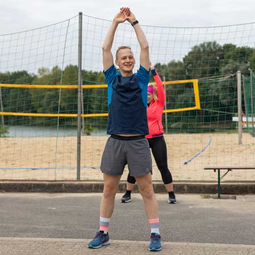 Zwei fröhliche Sportler dehnen sich vor dem Laufen am Strand, bereit für ein energiegeladenes Training. Angebote für Laufcoaching verfügbar!