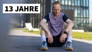 Ein Läufer in Sportkleidung sitzt entspannt auf dem Boden vor einem Bürogebäude, neben ihm steht der Text 13 Jahre als automatisch gespeicherter Entwurf.